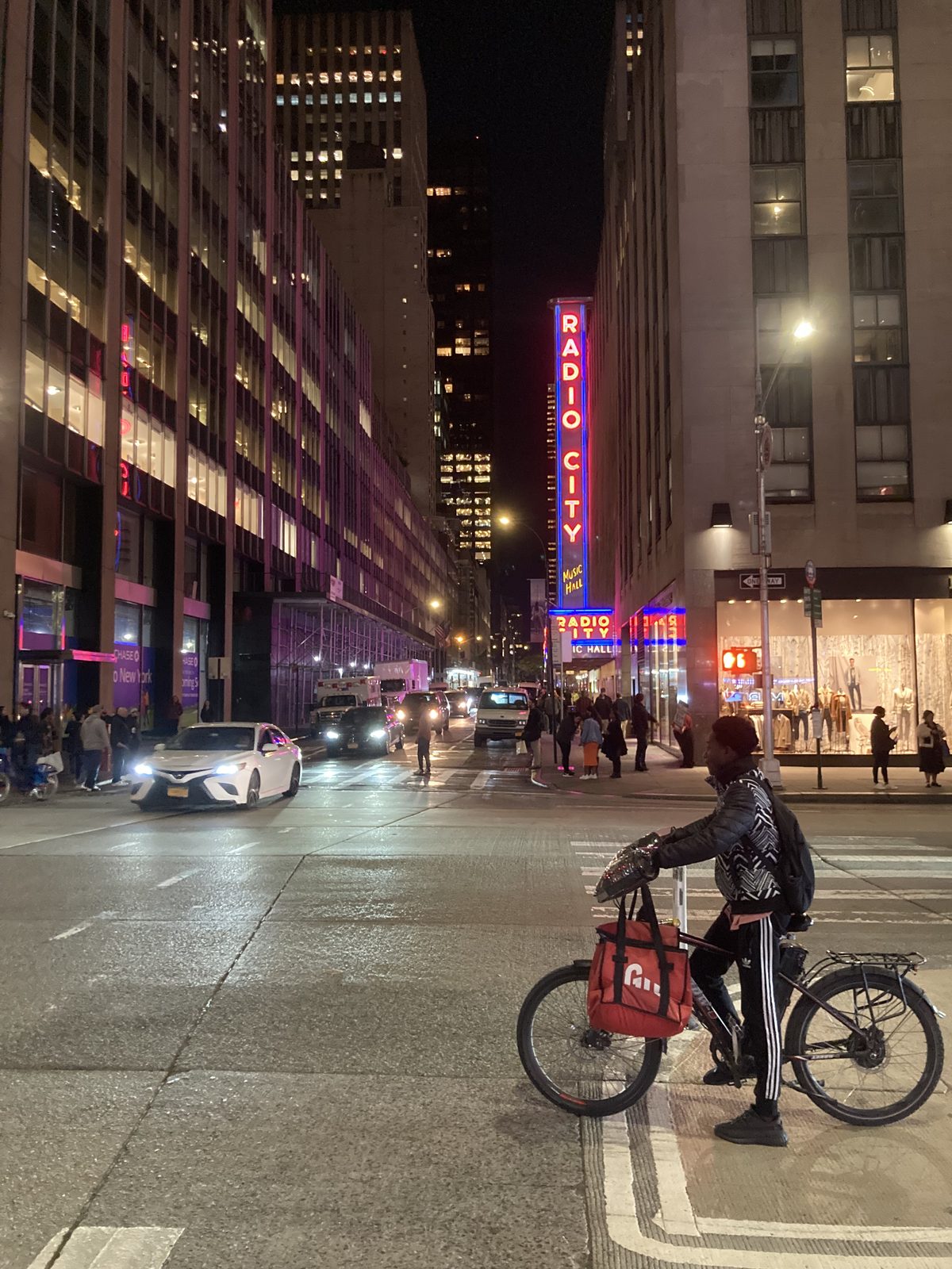 Radio City Music Hall marquee at night, delivery rider passing